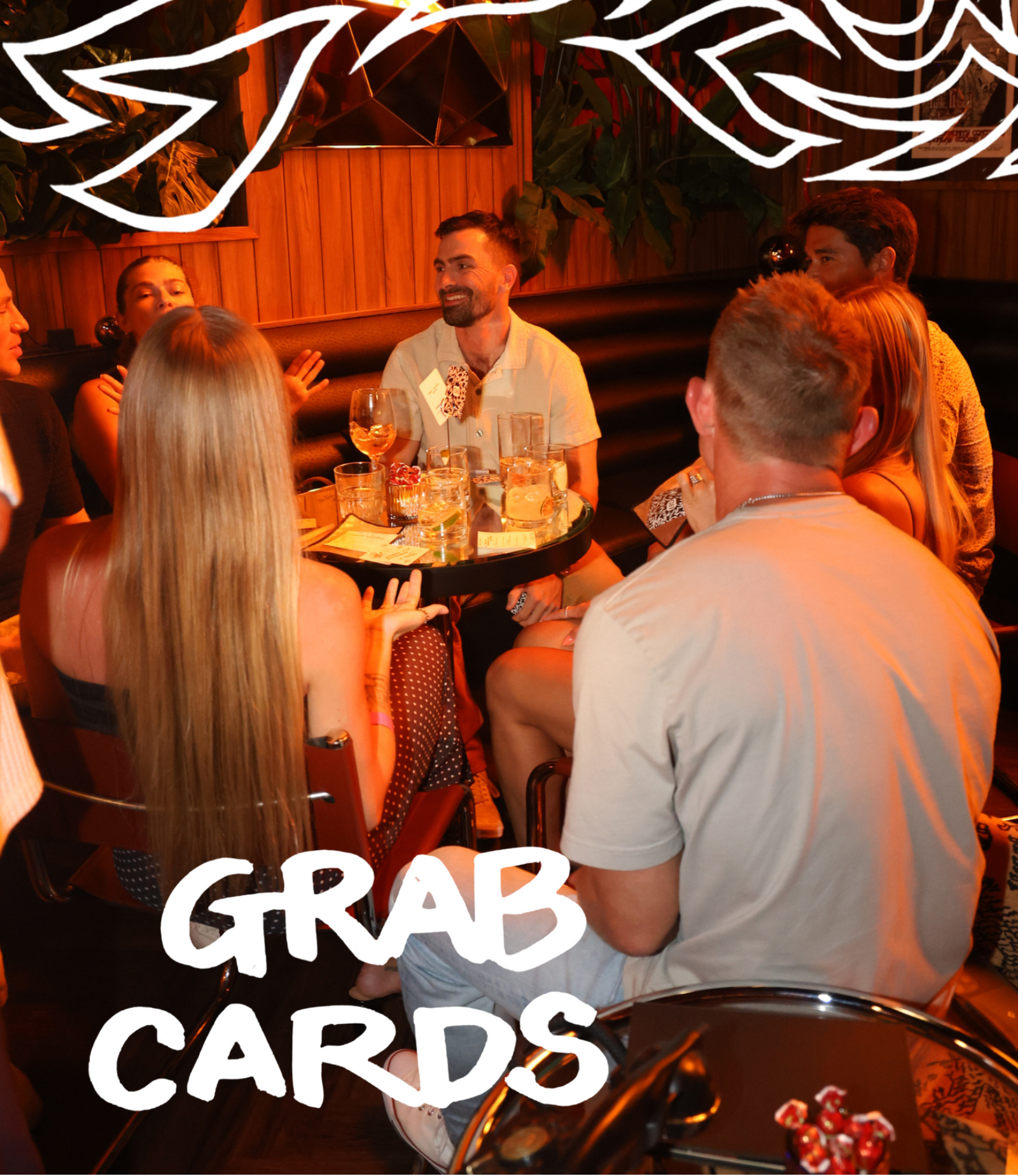 A group of people gathered around a table in a dimly lit bar or lounge, with large white text reading 'GRAB CARDS' overlaid at the bottom and abstract white line art at the top.